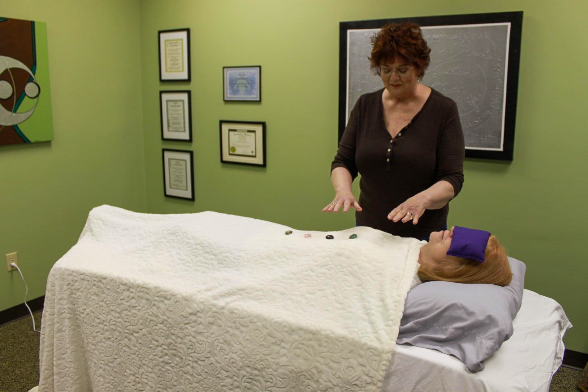 Kristi Pederson conducting an energy healing session, standing beside a client lying comfortably on a treatment table in a peaceful room.