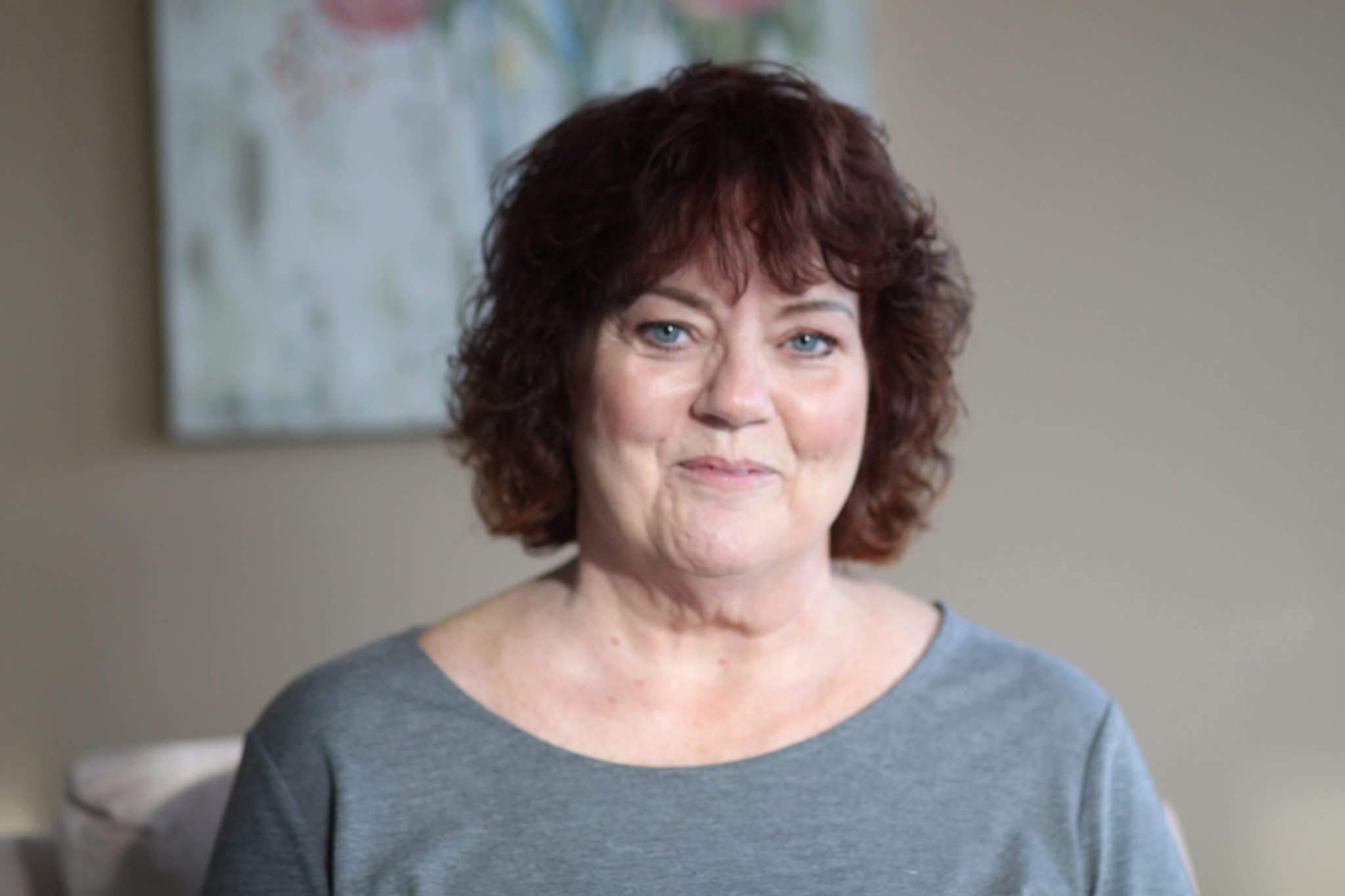 Portrait of Kristi Pederson smiling, seated indoors against a neutral background with soft lighting.