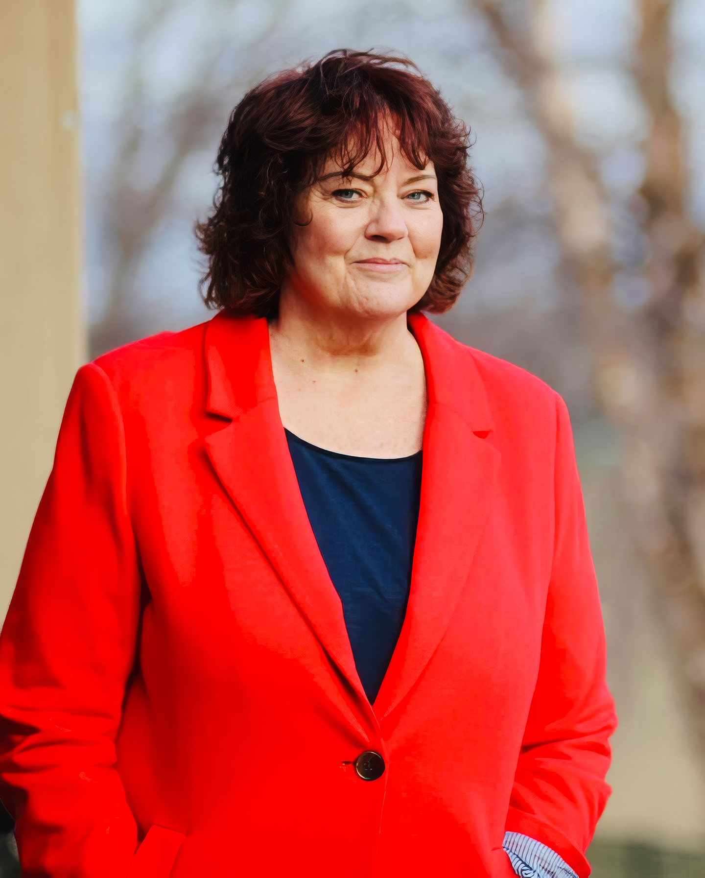 Kristi Pederson professional portrait Kristi Pederson in a red blazer, standing outdoors, confidently facing the camera.