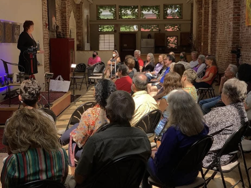 Kristi Pederson speaking on stage to a seated audience in an intimate indoor venue, engaging attendees during a live talk.